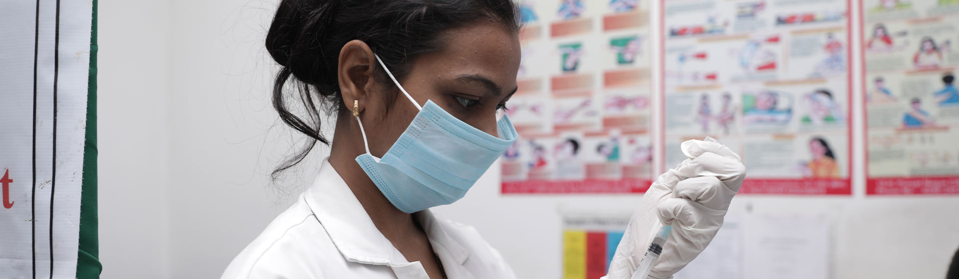 A female healthcare professional in a medical setting prepares a syringe for vaccination, demonstrating focus and adherence to safety protocols.