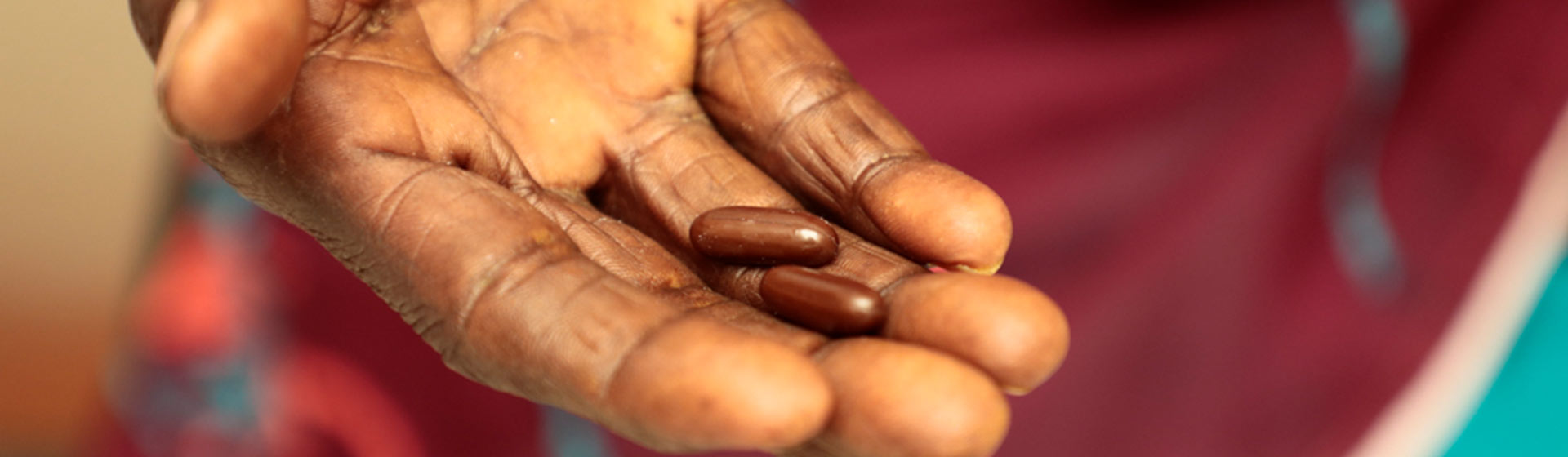 A person's hand displaying two medicinal capsules, emphasizing healthcare access and patient treatment.